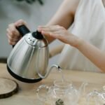 Modernus elektrinis virdulys pilantis vandenį į puodelį ant medinio stalo