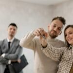 Jaunas asmuo laikantis raktus nuo naujų namų priešais modernų daugiabutį.