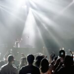 Ryškūs stroboskopų blyksniai muzikos renginio metu tamsioje salėje su dūmų efektais.